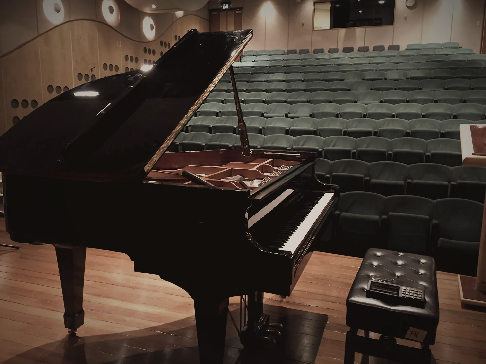 Black grand piano with its lid raised on an auditorium stage